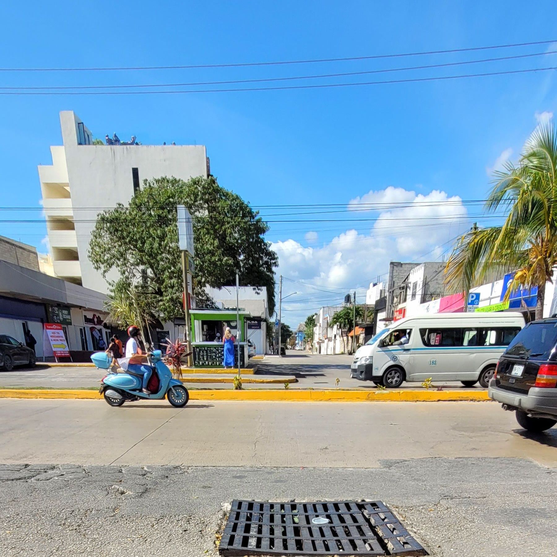 Busy street in Playa del Carmen with guagua or colectivo, car, and motorbikes passing by