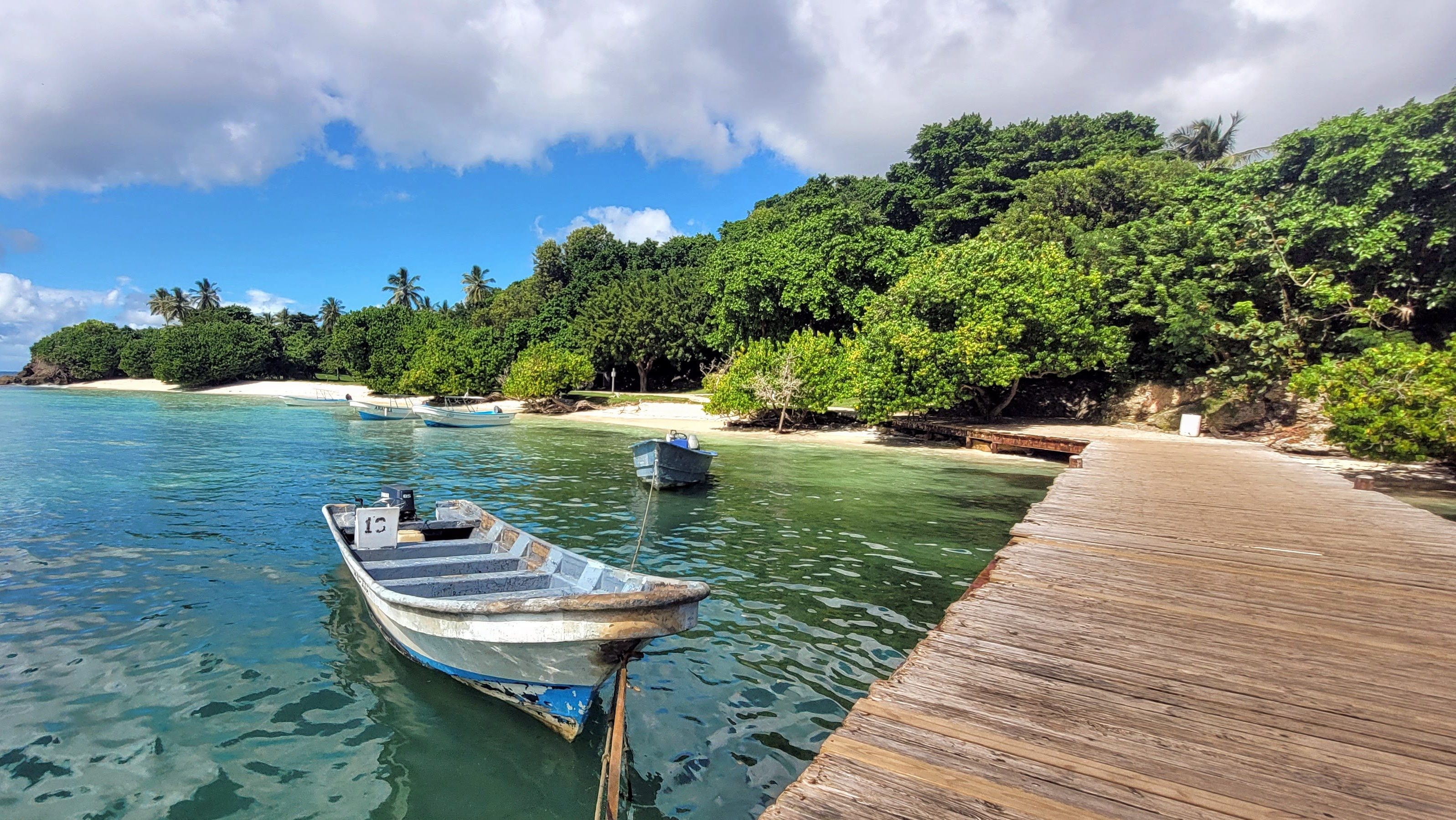 A serene view of Cayo Levantado, Samana with wooden boats anchored in turquoise water, surrounded by lush green vegetation and a sandy beach in the background.