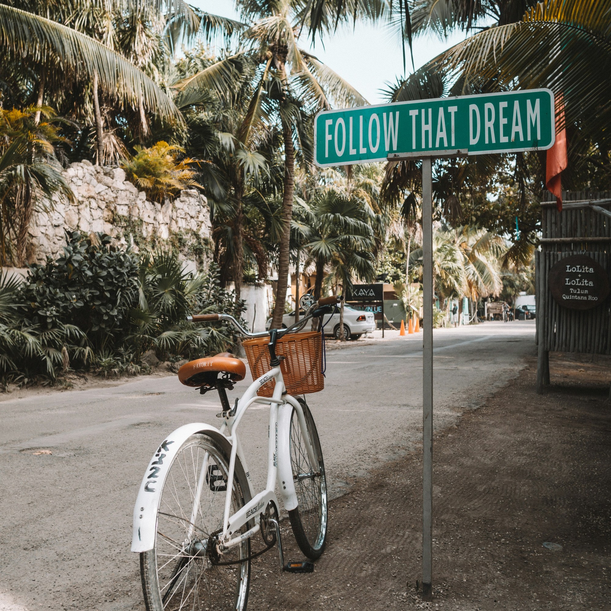 Bicycle near Follow That Dream sign on tree-lined street in Tulum, Mexico.