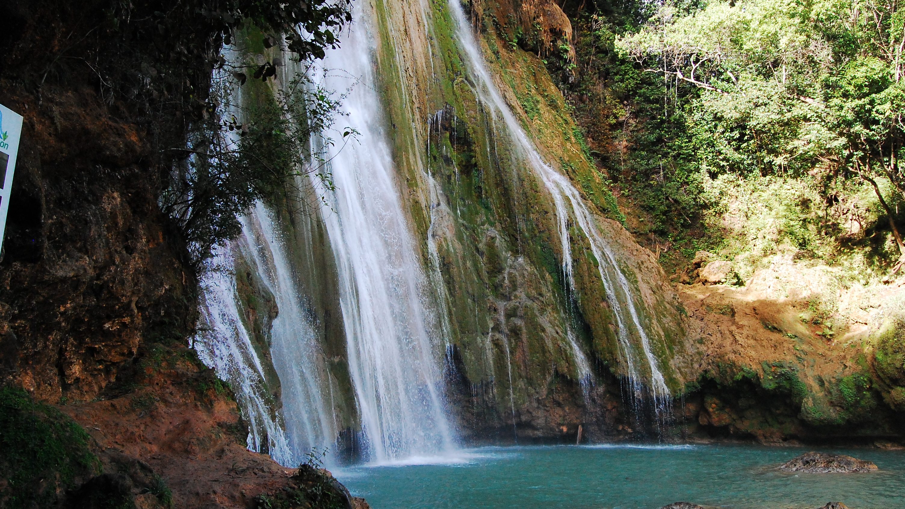 The beautiful El Limon waterfall cascading over rocky terrain into a serene turquoise pool, surrounded by lush green foliage.