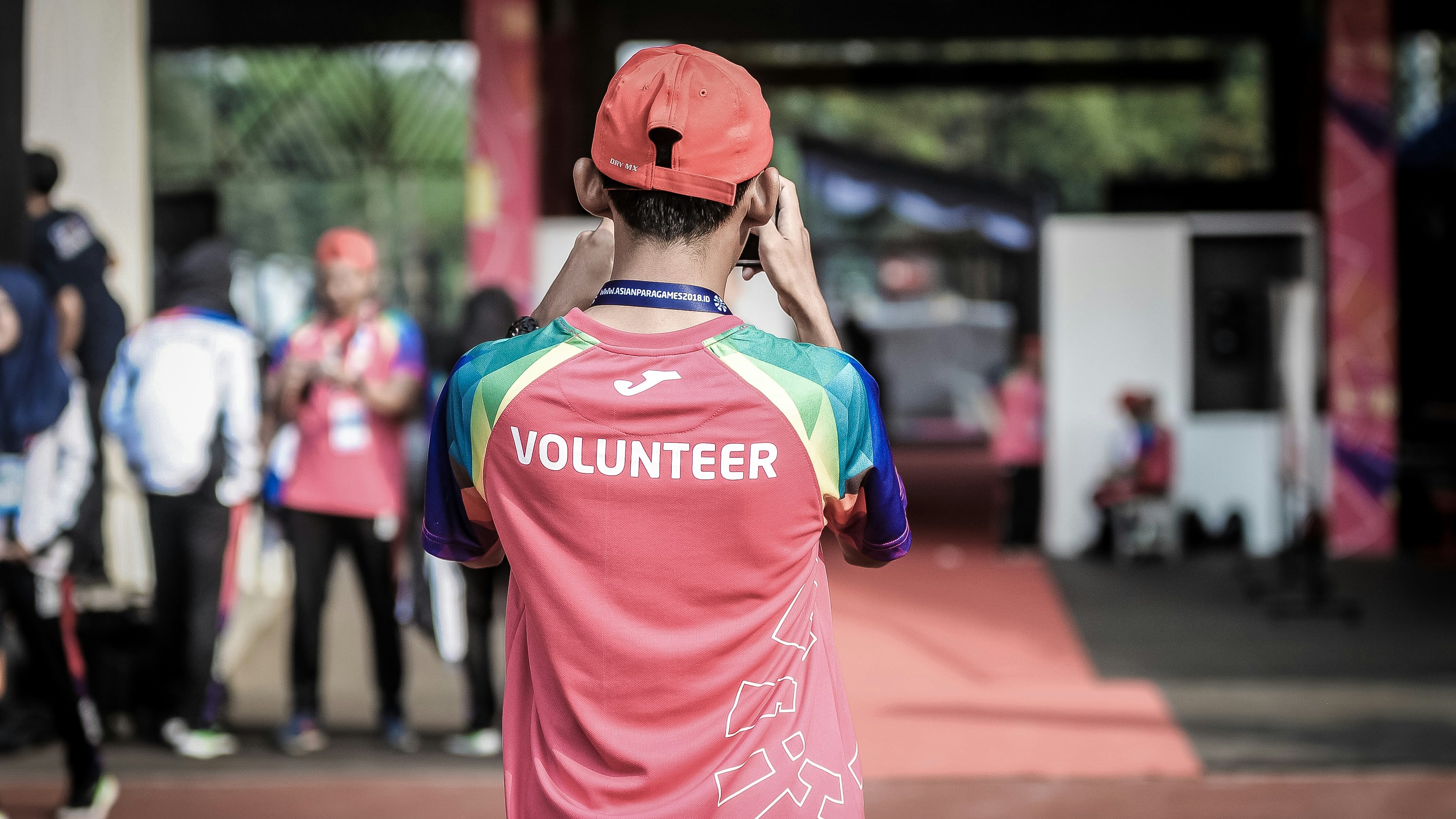 Young man wearing a volunteer shirt taking a photo with his phone, facing away from the camera.