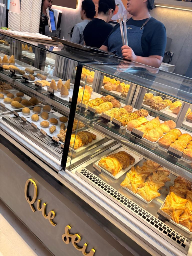 A display case filled with various baked goods, including pastries and cookies, with staff members preparing orders in the background.