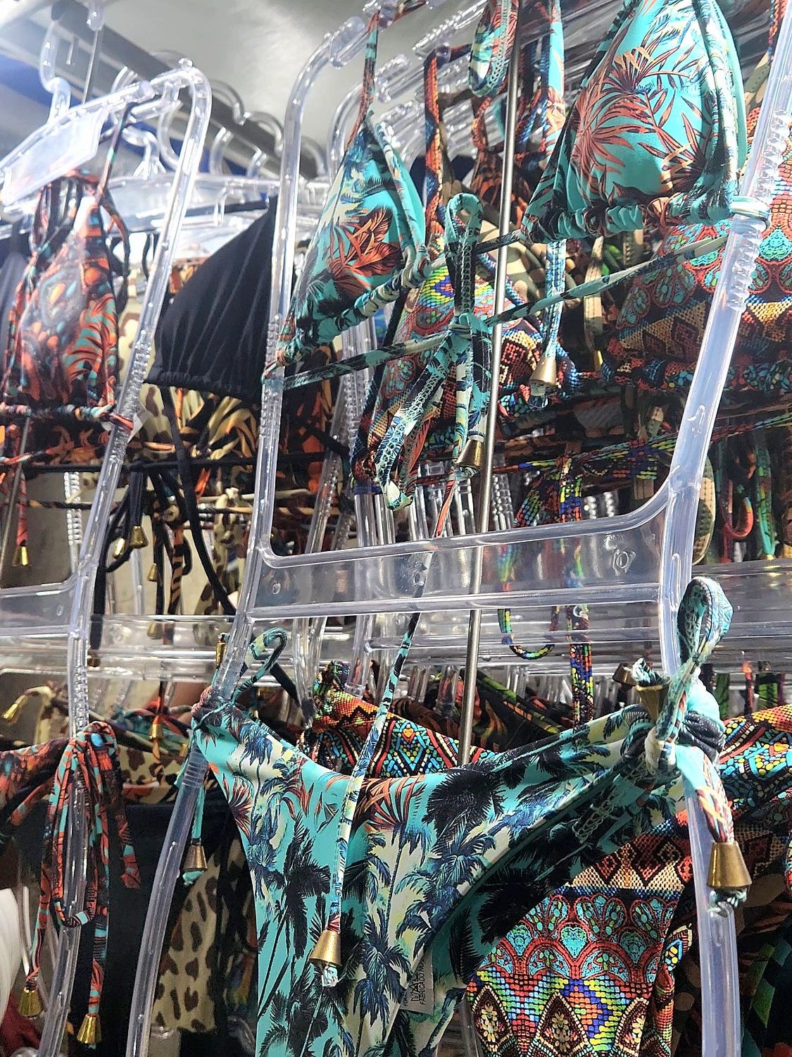 A display of colorful bikinis hanging on clear hangers, featuring various tropical patterns and designs. Sold from a market In Rio de Janeiro, Brazil.