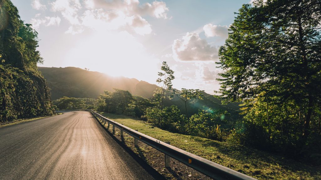 View of a road in the Dominican Republic from inside a car, with trees lining the roadside and mountains in the distance